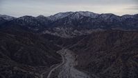 5K stock footage aerial video fly over a dry riverbed toward rock formations and snowy mountains at twilight, San Gabriel Mountains, California Aerial Stock Footage | AX0008_003