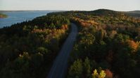 5.5K stock footage aerial video flying over a road among colorful forest in autumn, Stockton Springs, Maine, sunset Aerial Stock Footage | AX149_118