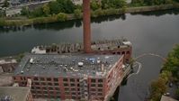 5.5K stock footage aerial video orbiting away from an abandoned factory and smoke stack along the river, autumn, Lowell, Massachusetts Aerial Stock Footage | AX152_131
