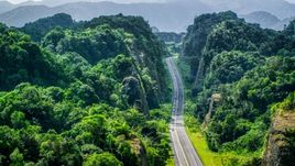 A highway cutting through lush green mountains, Karst Forest, Puerto Rico Aerial Stock Photos | AX101_085.0000000F