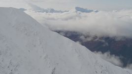4K aerial stock footage rounding snowy summit, reveal cloud covered Kenai Mountains, Alaska Aerial Stock Footage | AK0001_0528