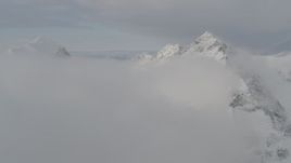 4K aerial stock footage flying by a snow covered peak, low clouds, Chugach Mountains, Alaska Aerial Stock Footage | AK0001_0561
