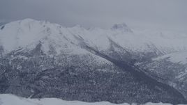 4K aerial stock footage flying over snowy summit revealing wooded valley, Chugach Mountains, Alaska Aerial Stock Footage | AK0001_1174