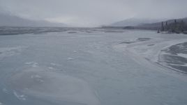 4K aerial stock footage following an icy river toward snowy, wooded shoreline, Knik River Valley, Alaska Aerial Stock Footage | AK0001_1267