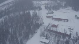4K aerial stock footage flying over forest and small warehouse buildings to reveal Eagle River Road overpass, falling snow, Alaska Aerial Stock Footage | AK0001_1316