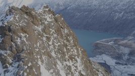 4K aerial stock footage flying over a rocky, snow covered peak revealing Eklutna Lake, Alaska Aerial Stock Footage | AK0001_1353