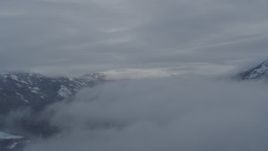 4K aerial stock footage flying between clouds over Eklutna Lake Valley, Alaska in snow Aerial Stock Footage | AK0001_1553