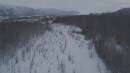 4K aerial stock footage flying over snow covered, wooded riverbank into the Knik River Valley, Alaska Aerial Stock Footage | AK0001_1593