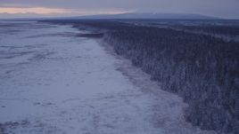 4K aerial stock footage flying over frozen, snowy ground beside forest at twilight, Point MacKenzie, Alaska Aerial Stock Footage | AK0001_1694