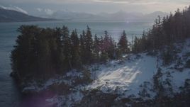 4K aerial stock footage flying over snowy, wooded shore to sun reflected water in Port Wells, Alaska Aerial Stock Footage | AK0001_1836