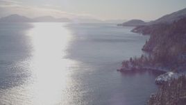 4K aerial stock footage he sun reflecting off of water in Port Wells next to snowy, wooded shore, Alaska Aerial Stock Footage | AK0001_1838