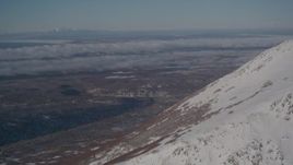 4K aerial stock footage video flying by snowy mountain peak toward wooded foothills near Anchorage, Alaska Aerial Stock Footage | AK0001_2002