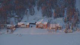 4K aerial stock footage flying away from snow covered houses on Lucile Lake at sunset, Wasilla, Alaska Aerial Stock Footage | AK0001_2086