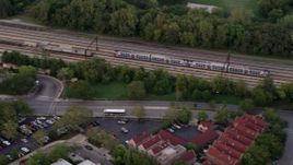 4.8K aerial stock footage of tracking a commuter train traveling through Kenwood at twilight, reveal apartments and strip mall, Chicago, Illinois Aerial Stock Footage | AX0003_022