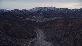 5K aerial stock footage fly over a dry riverbed toward rock formations and snowy mountains at twilight, San Gabriel Mountains, California Aerial Stock Footage | AX0008_003