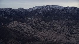 5K aerial stock footage tilt from dry riverbed to reveal rock formations and snowy San Gabriel Mountains at twilight, California Aerial Stock Footage | AX0008_004