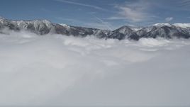 5K aerial stock footage fly over clouds to approach snowy San Bernardino Mountains in winter, California Aerial Stock Footage | AX0009_107
