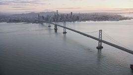 6K aerial stock footage panning across the Bay Bridge to reveal the Downtown San Francisco skyline at sunset, California Aerial Stock Footage | AX0174_0086