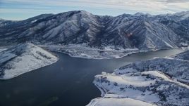 5.5K aerial stock footage an icy reservoir with snowy Wasatch Range mountains on the shore in winter, Utah Aerial Stock Footage | AX126_230E