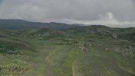 5.5K aerial stock footage of flying by green hills, trees, heavy clouds above, Wasatch Range, Utah Aerial Stock Footage | AX130_127E