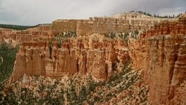 5.5K aerial stock footage of flying away from hoodoos, mesa cliff, tree-covered slopes, Bryce Canyon National Park, Utah Aerial Stock Footage | AX130_464E