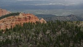 5.5K aerial stock footage of flying by top of butte, forest, distant valley, Bryce Canyon National Park, Utah Aerial Stock Footage | AX131_011