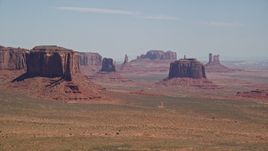5.5K aerial stock footage of passing by rugged mesas and buttes in a hazy desert valley, Monument Valley, Utah, Arizona Aerial Stock Footage | AX135_182E