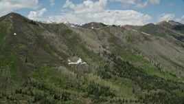 5.5K aerial stock footage focus on a Tecnam P2006T passing a green mountain, aspen trees, snow patches, Wasatch Range, Utah Aerial Stock Footage | AX140_141E
