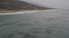 5K aerial  video fly low over the ocean to pass surfers waiting for waves near the shore, Malibu, California Aerial Stock Footage | AX42_081