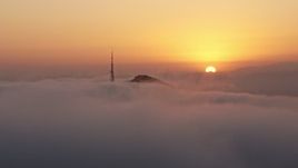 4K aerial stock footage of the sunset behind Hollywood Hills, radio tower covered in Marine Layer, California Aerial Stock Footage | AX44_031