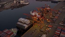 5K aerial stock footage of flying over cargo ships laden with containers docked beneath cranes at the Port of Seattle, Washington, sunset Aerial Stock Footage | AX50_068E