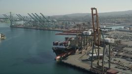 4.8K aerial stock footage of passing a cargo ship with containers beneath cranes at the Port of Los Angeles, California Aerial Stock Footage | AX68_170