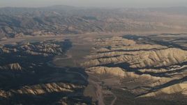 4K aerial stock footage Farms beyond a dry riverbed between rugged mountain ridges at sunrise, Cuyama, California Aerial Stock Footage | AX70_027