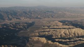 4K aerial stock footage Dry riverbed between mountain ridges near farms at sunrise, Cuyama, California Aerial Stock Footage | AX70_028