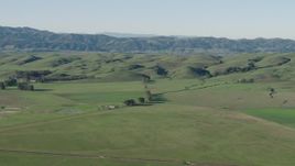 4K aerial stock footage Passing by farm fields beside green hills in Hollister, California Aerial Stock Footage | AX70_110