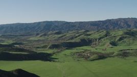 4K aerial stock footage Fly over a green hill to reveal a valley and mountains in Hollister, California Aerial Stock Footage | AX70_125