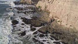 5K aerial stock footage of tilt from cliffs to waves rolling into rock formations, Avila Beach, California Aerial Stock Footage | AXSF02_050