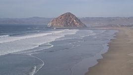 5K aerial stock footage flying low over the beach and ocean waves toward Morro Rock, Morro Bay, California Aerial Stock Footage | AXSF03_001