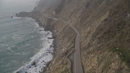 5K aerial stock footage of following Highway 1 coastal road on cliffs, tilt to a bird's eye view of a car on the road, Big Sur, California Aerial Stock Footage | AXSF03_090