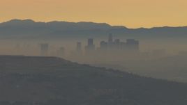 HD aerial stock footage of smoggy skyline beyond hills, Downtown Los Angeles, California, sunset Aerial Stock Footage | CBAX01_068