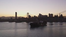 5K aerial stock footage of a cargo ship sailing under Bay Bridge near Downtown San Francisco skyline, California, sunset Aerial Stock Footage | DFKSF10_053