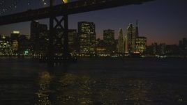 5K aerial stock footage of flying under the Bay Bridge toward Ferry Building and skyscrapers in Downtown San Francisco, California, night Aerial Stock Footage | DFKSF10_100
