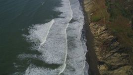 5K aerial stock footage of a reverse view of ocean waves rolling toward a beach and coastal cliffs, Lakeshore District, San Francisco, California Aerial Stock Footage | DFKSF15_047