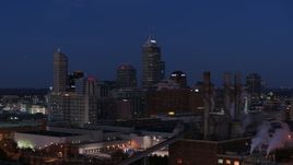 5.7K aerial stock footage of giant skyscrapers of the city skyline at twilight, seen from factory smoke stacks, Downtown Indianapolis, Indiana Aerial Stock Footage | DX0001_002973