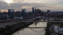 5.7K aerial stock footage the city's skyline and bridges seen while passing the Cumberland River at sunset, Downtown Nashville, Tennessee Aerial Stock Footage | DX0002_119_038