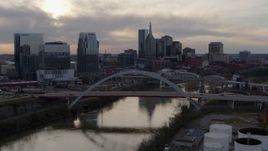 5.7K aerial stock footage the city's skyline while descending past bridges over the Cumberland River at sunset, Downtown Nashville, Tennessee Aerial Stock Footage | DX0002_119_039
