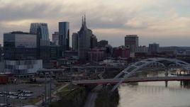 5.7K aerial stock footage riverfront skyline seen while passing bridge on Cumberland River at sunset, Downtown Nashville, Tennessee Aerial Stock Footage | DX0002_120_003