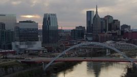 5.7K aerial stock footage of the riverfront skyline, ascend past bridge spanning the river at sunset, Downtown Nashville, Tennessee Aerial Stock Footage | DX0002_120_012