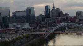 5.7K aerial stock footage of the riverfront skyline while passing bridge spanning the river at sunset, Downtown Nashville, Tennessee Aerial Stock Footage | DX0002_120_013