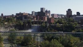 5.7K aerial stock footage approach the city's skyline behind waterfalls and river from bridge, Downtown Rochester, New York Aerial Stock Footage | DX0002_206_031